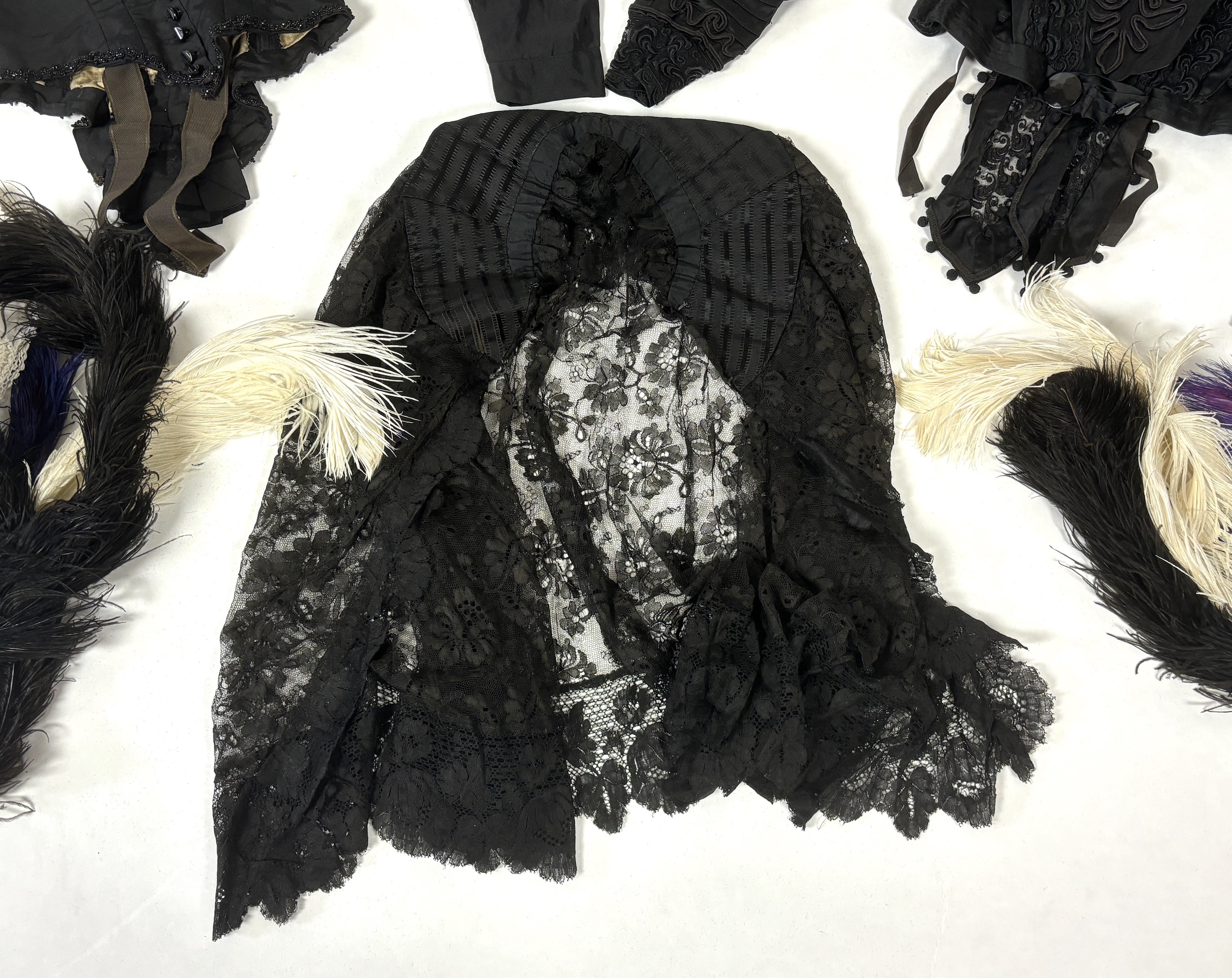 Two ladies Victorian black satin and lace, bead trimmed bodices, together with a black lace cape, a black satin cape, a small collection of coloured feathers and a child’s white worked pinafore